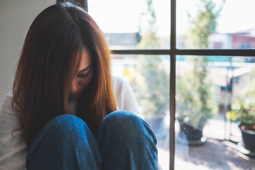 Person experiencing neurological symptoms from mold exposure near window