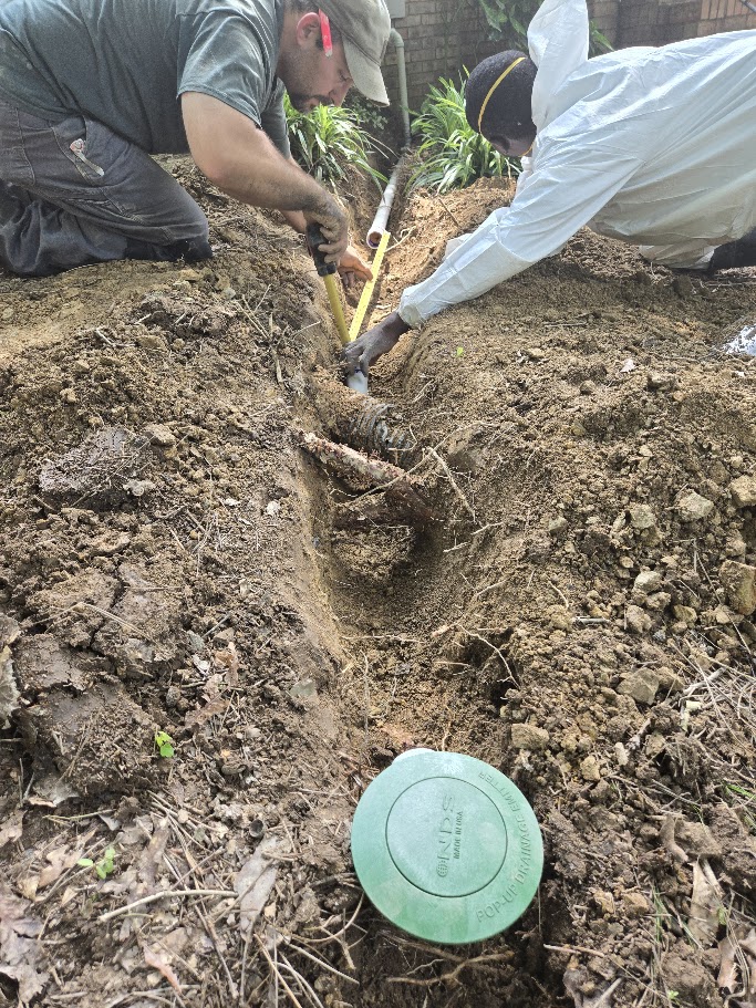 Workers fixing pipe in soil, ensuring water drainage.