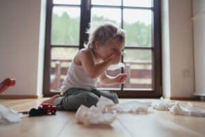 Sick child with tissues indoors near a window.